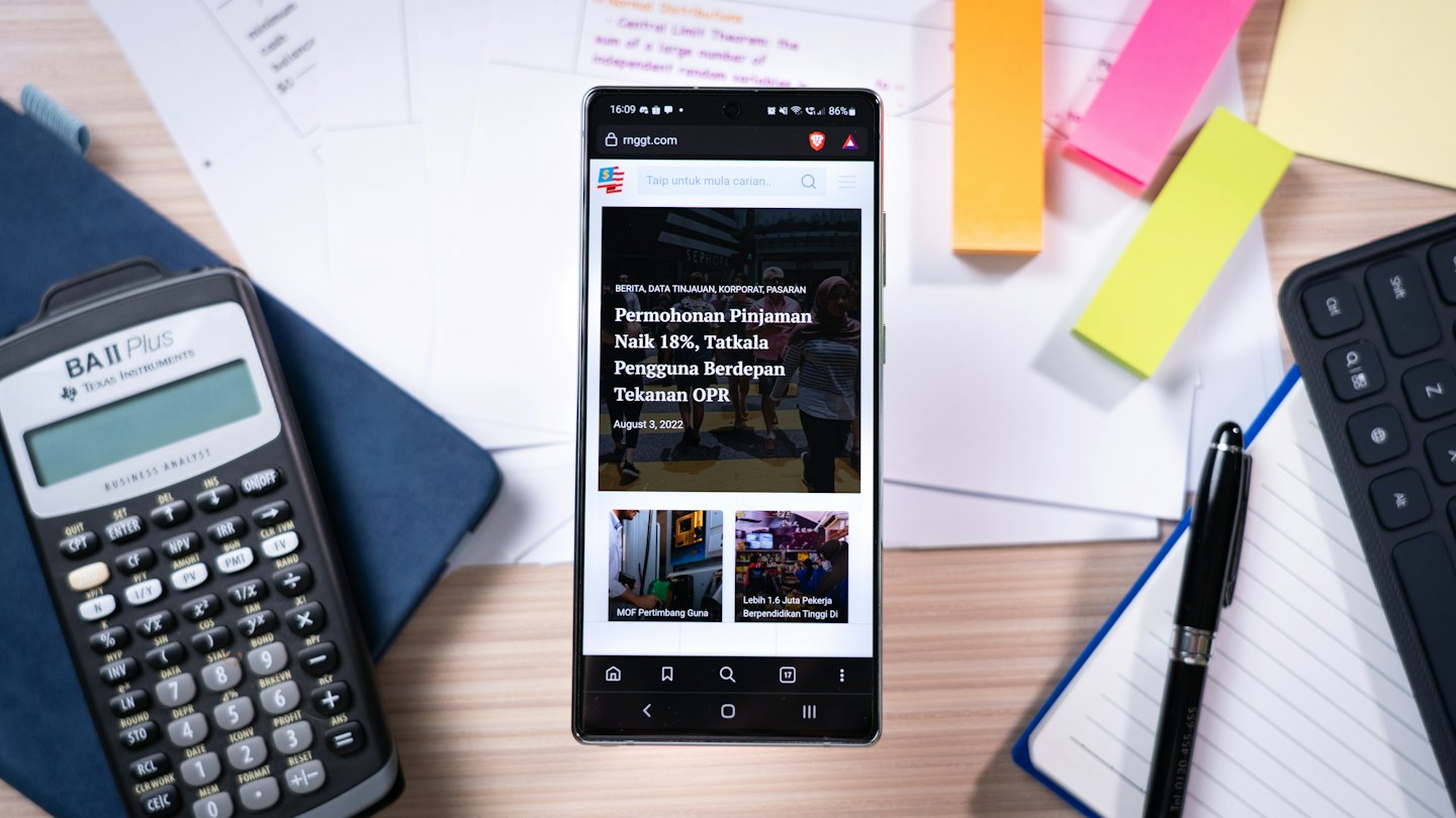 Smartfon wyświetlający wiadomości biznesowe na drewnianym biurku z artykułami biurowymi.