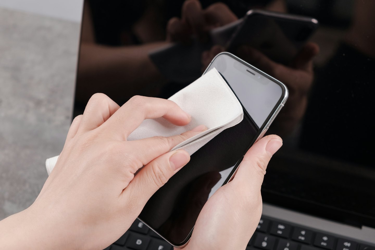 Dłoń przeciera ekran smartfona białą ściereczką.